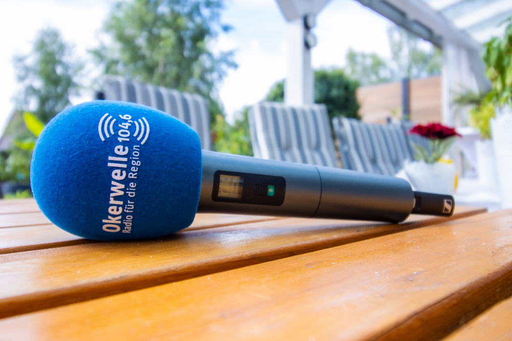Ein Mikrofon mit der Aufschrift "Okerwelle" liegt auf einem Tisch in einem Garten.